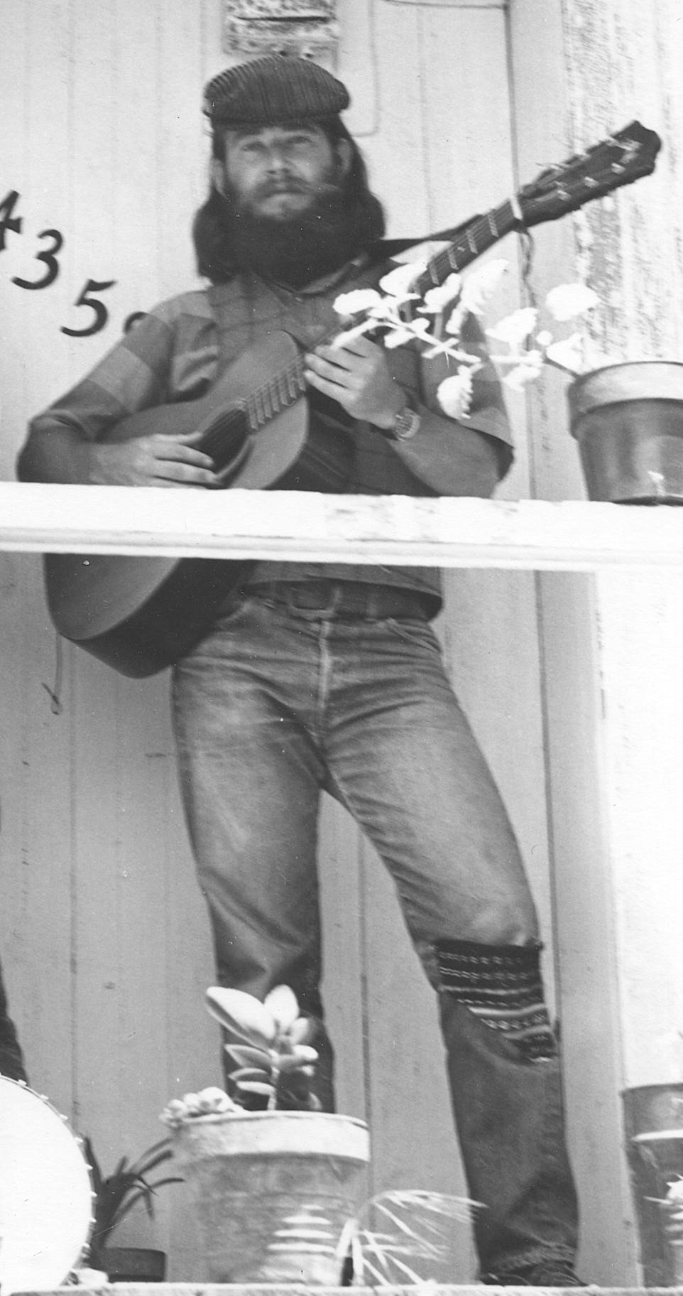 Ryan Thomson poses with a Guild guitar on Pam Ostergren and David Brown's porch in La Mesa, California, 1974. Ryan, Dave, and Pam are members of the Chicken Cheek Tweakers old time string band